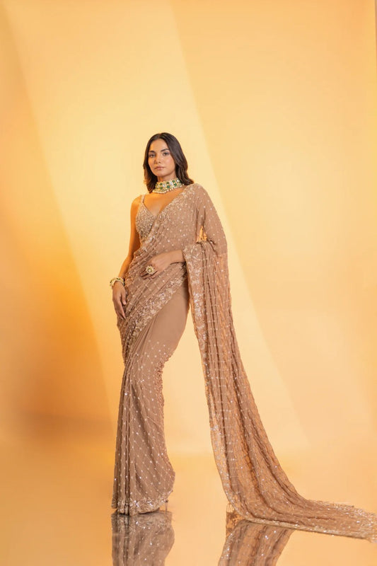 Champagne tulle blouse embroidered with sequins, buggle beads and crystals with tassel droplets at waist & crystal embellishments on shoulders, and hand embroidered georgette saree adorned with tassels at pallu, along with a satin petticoat.