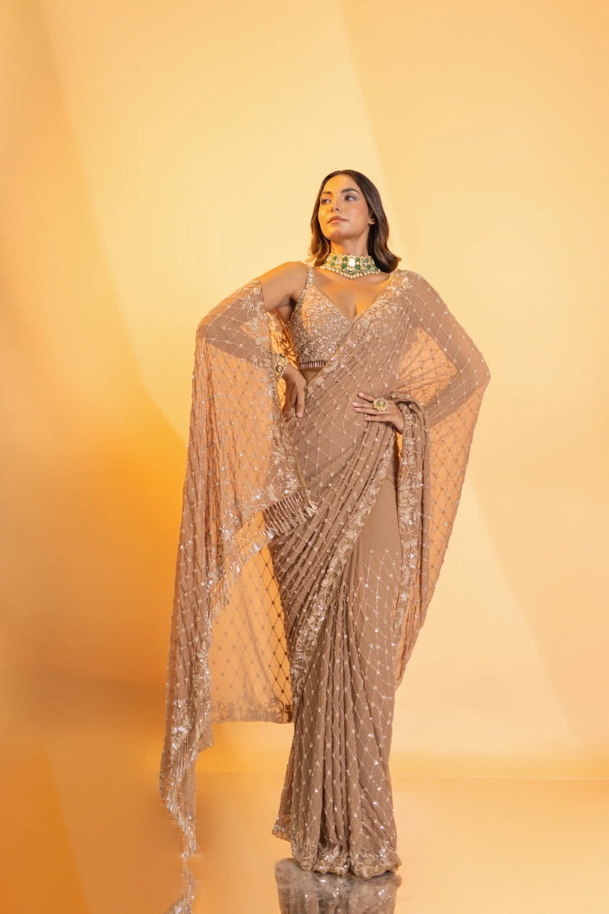 Champagne tulle blouse embroidered with sequins, buggle beads and crystals with tassel droplets at waist & crystal embellishments on shoulders, and hand embroidered georgette saree adorned with tassels at pallu, along with a satin petticoat.